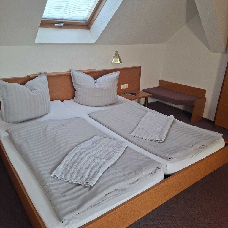 Helle, gemütliche Zimmer mit zwei Betten, Kissen und einer Sitzecke. Dachfenster vorhanden.