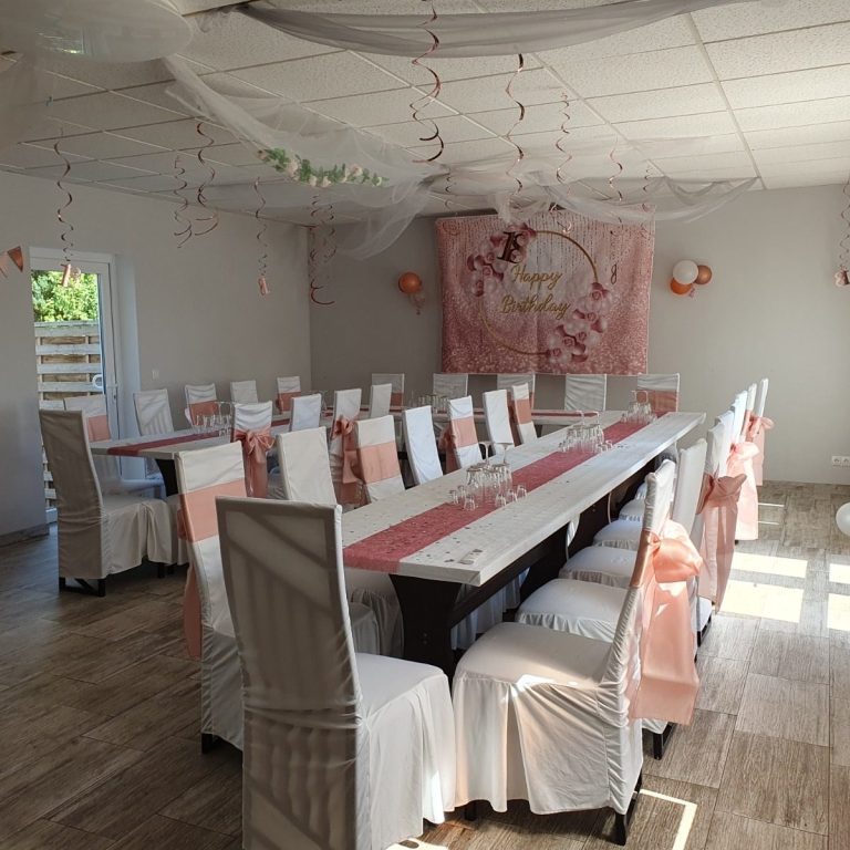 Festlich dekorierter Veranstaltungsraum mit Tischen und Stühlen in Weiß und Rosa.