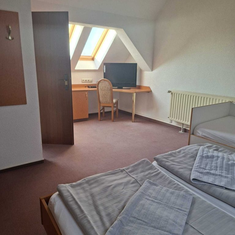 Helles Gästezimmer mit Dachfenstern, Schreibtisch und Bett.
