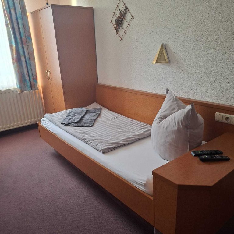 Ein einfaches Zimmer mit einem Einzelbett, Kissen, einer Decke und einem Fernseher.